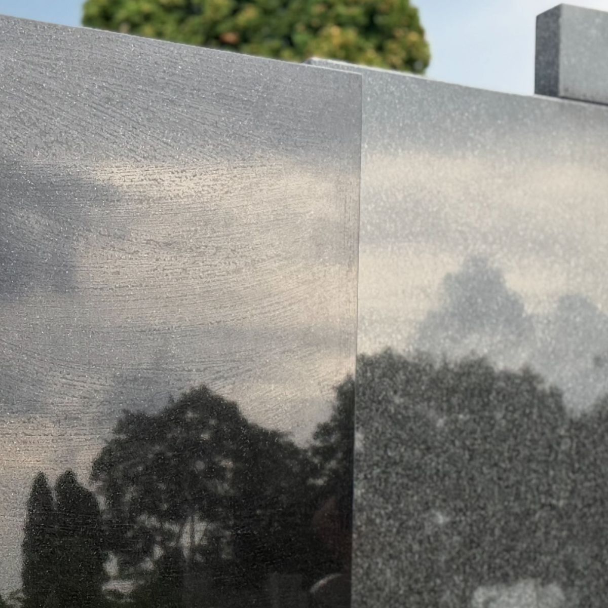 Czarny granit Monumental wypolerowany na lustro, odbijają się w nim chmury i drzewa